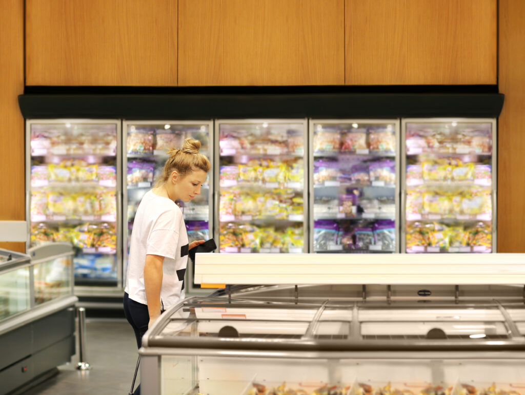 Customer shopping frozen food near commercial coolers in a grocery store setting